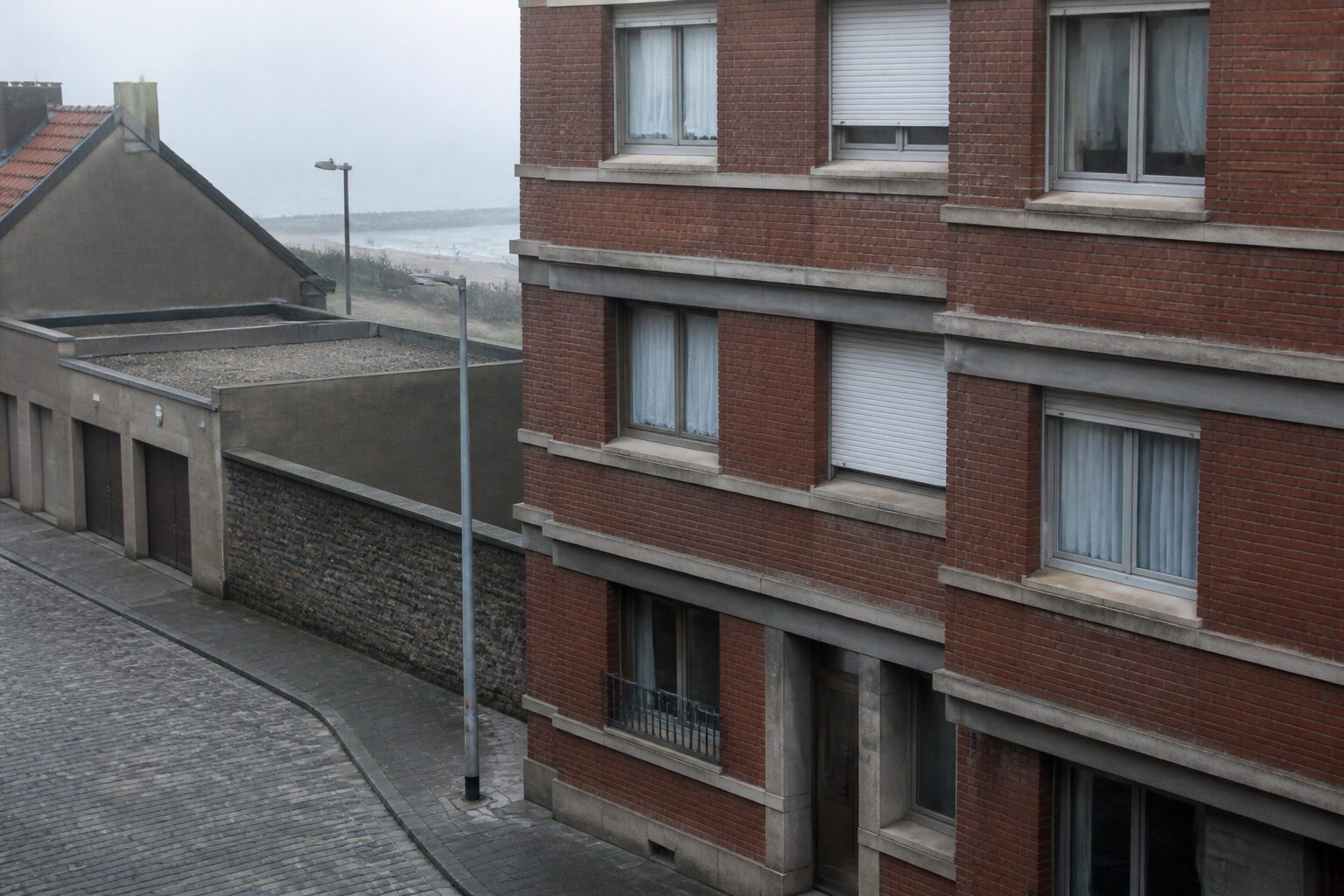 Immeuble en brique calaisien avec rue pavée et mer en arrière-plan