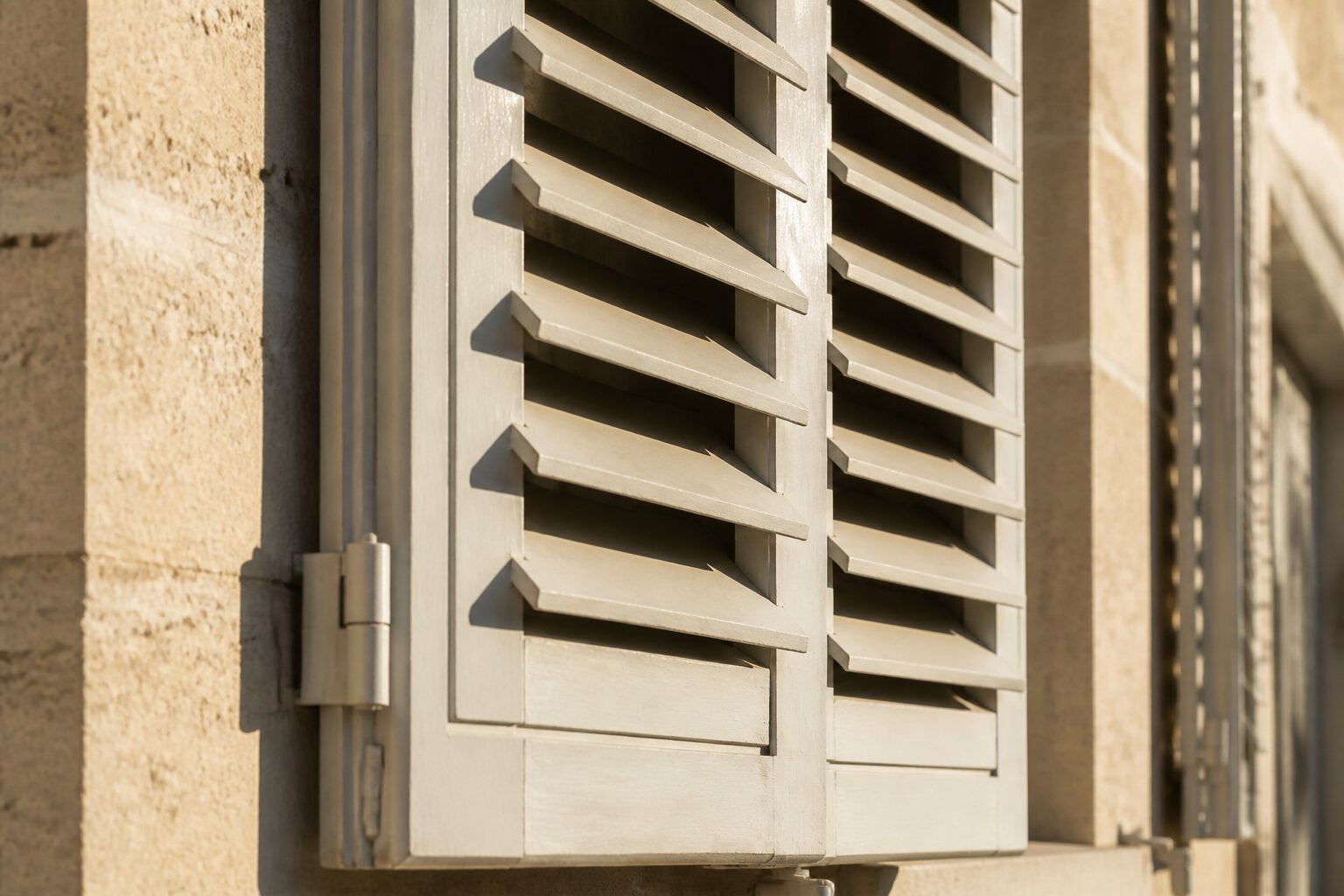Volets en bois d'une façade ensoleillée, mi-fermés pour filtrer la chaleur estivale