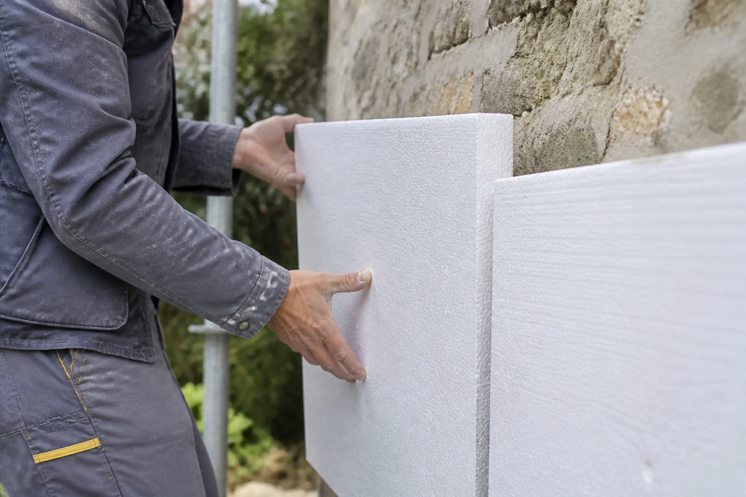Artisan posant un isolant sur un mur extérieur, chantier de rénovation en France