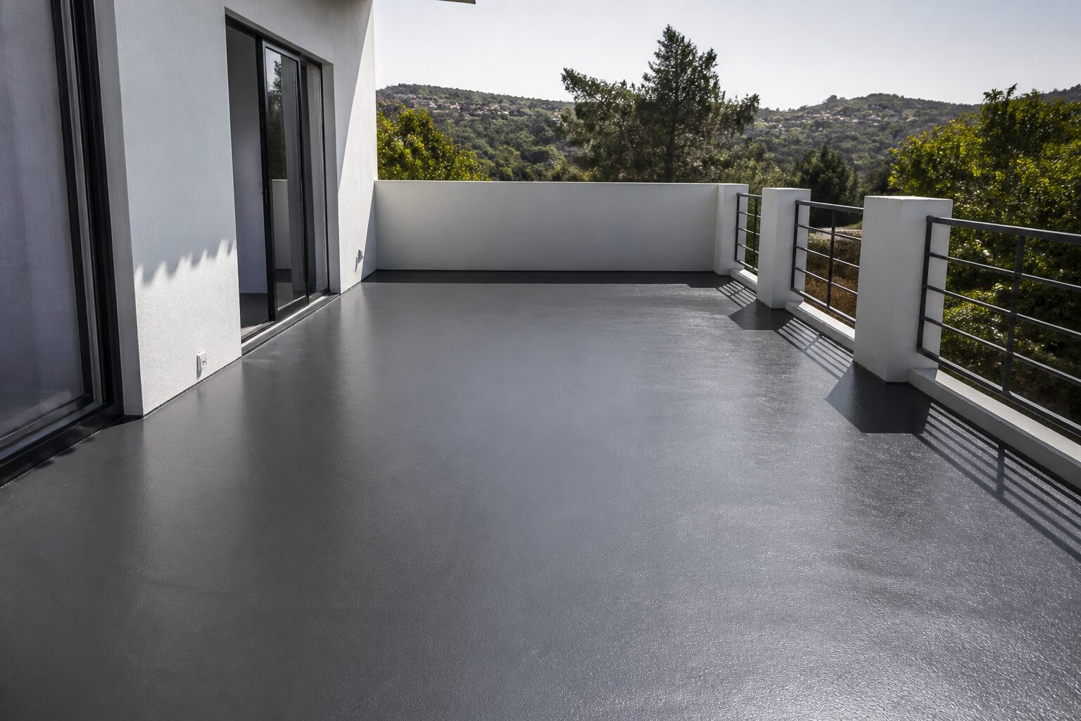 Terrasse en béton extérieur fraîchement peinte, sol gris anthracite uniforme sous une lumière naturelle de jardin