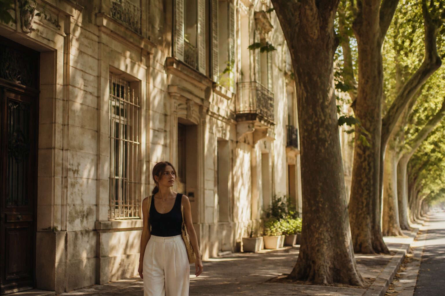 Vue d'une rue résidentielle calme d'une ville du sud de la France, façades en pierre beige, trottoir ombragé par des platanes, lumière dorée