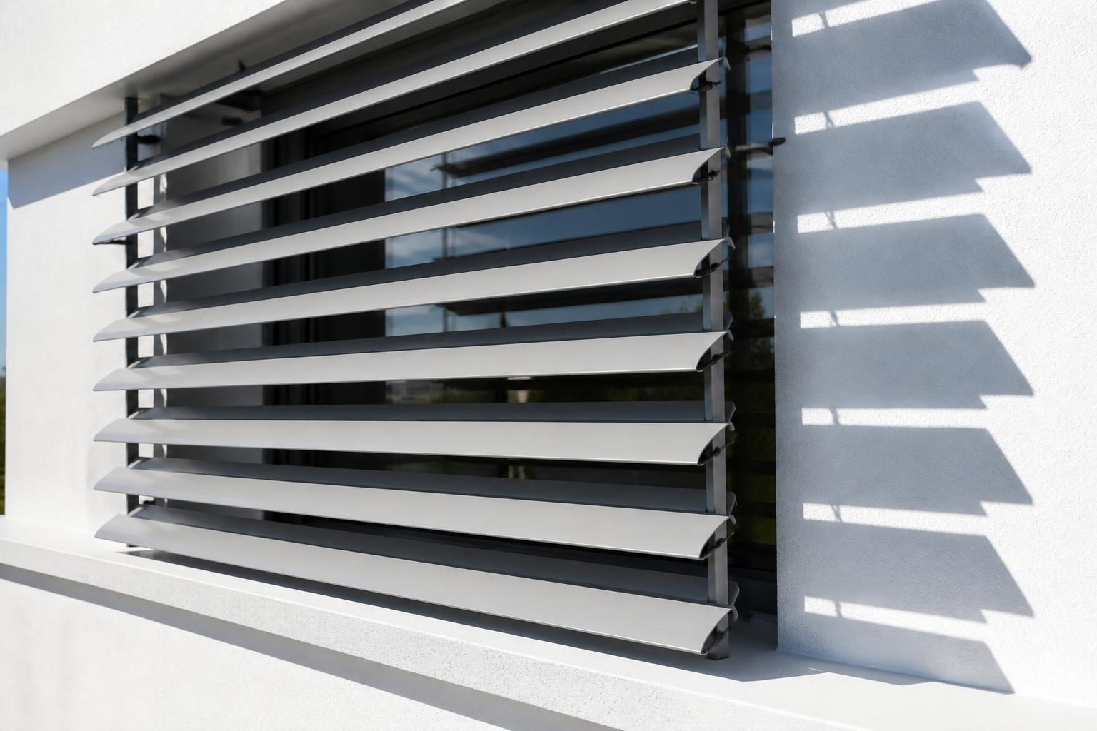 Brise-soleil orientable aux lames inclinées devant une fenêtre en plein soleil